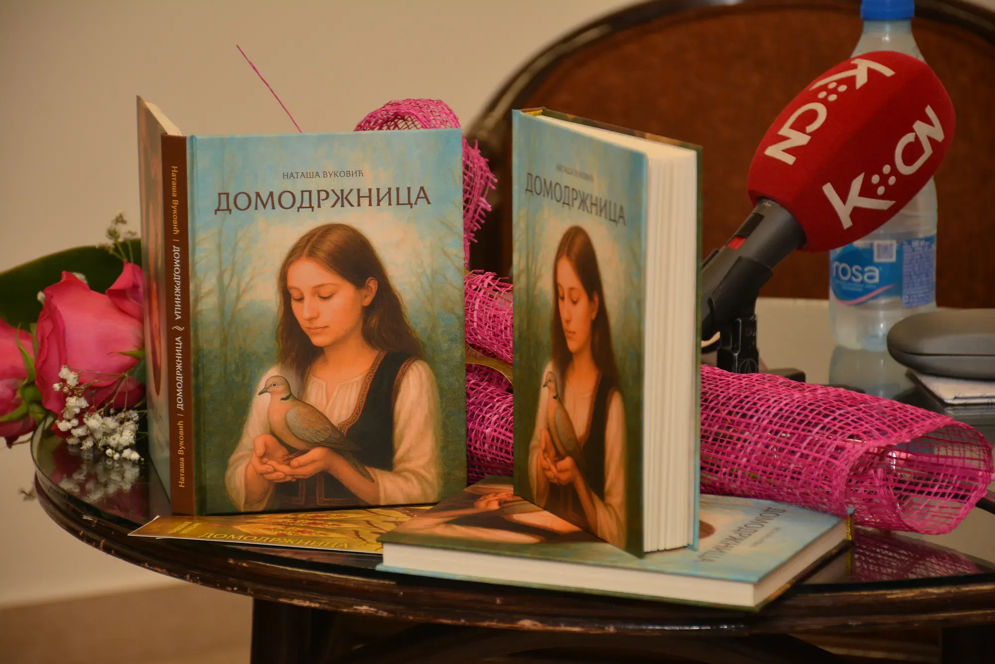 Примерци књиге „Домодржница“ Наташе Вуковић и микрофон на столу пред промоцију у Рашки